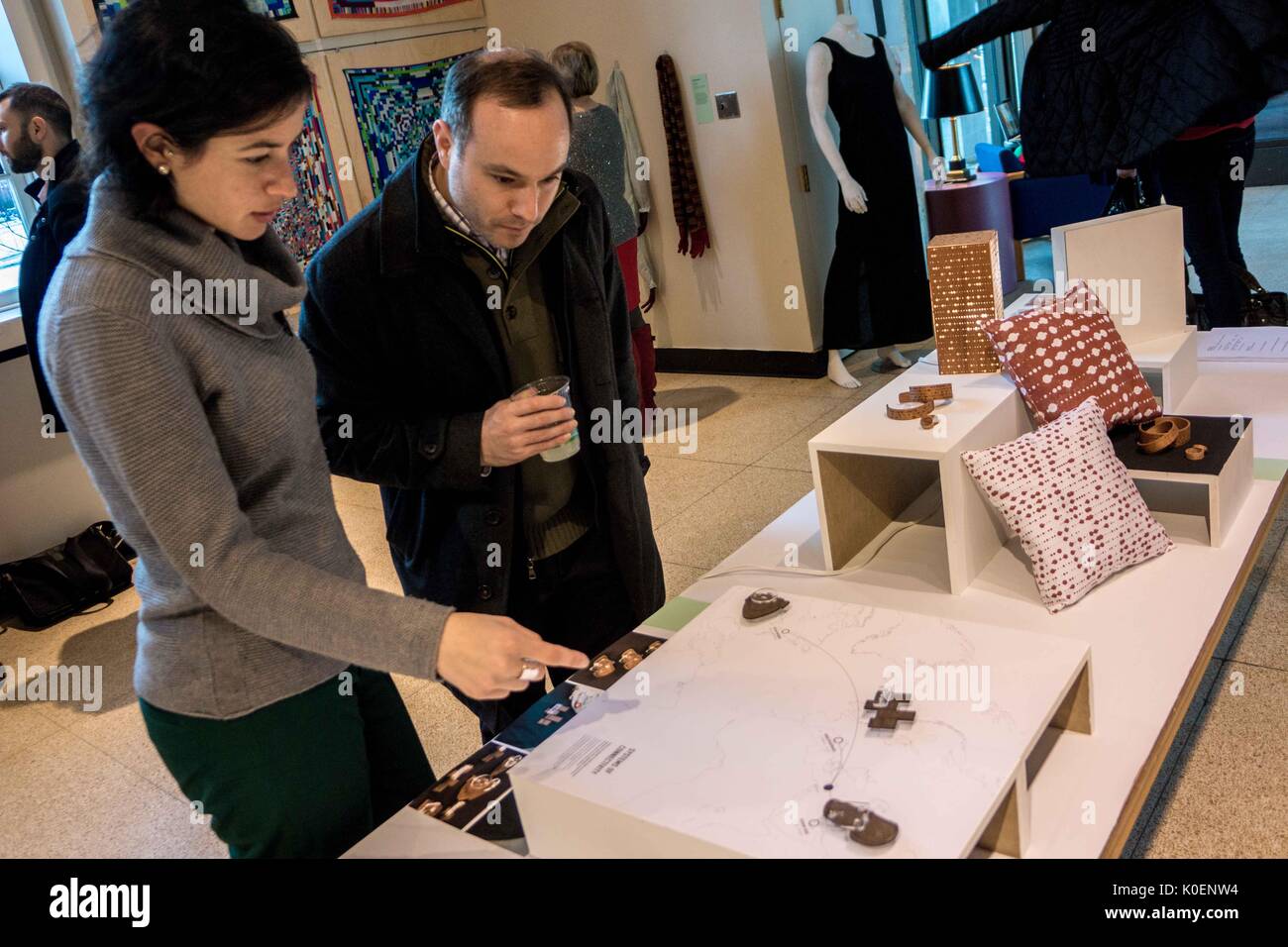 Two adults look down at a small art display on a long table filled with more displays, the woman points to something in the display at the Unravel the Code Opening at The Johns Hopkins University Sheridan Libraries, 2016. Courtesy Eric Chen. Stock Photo