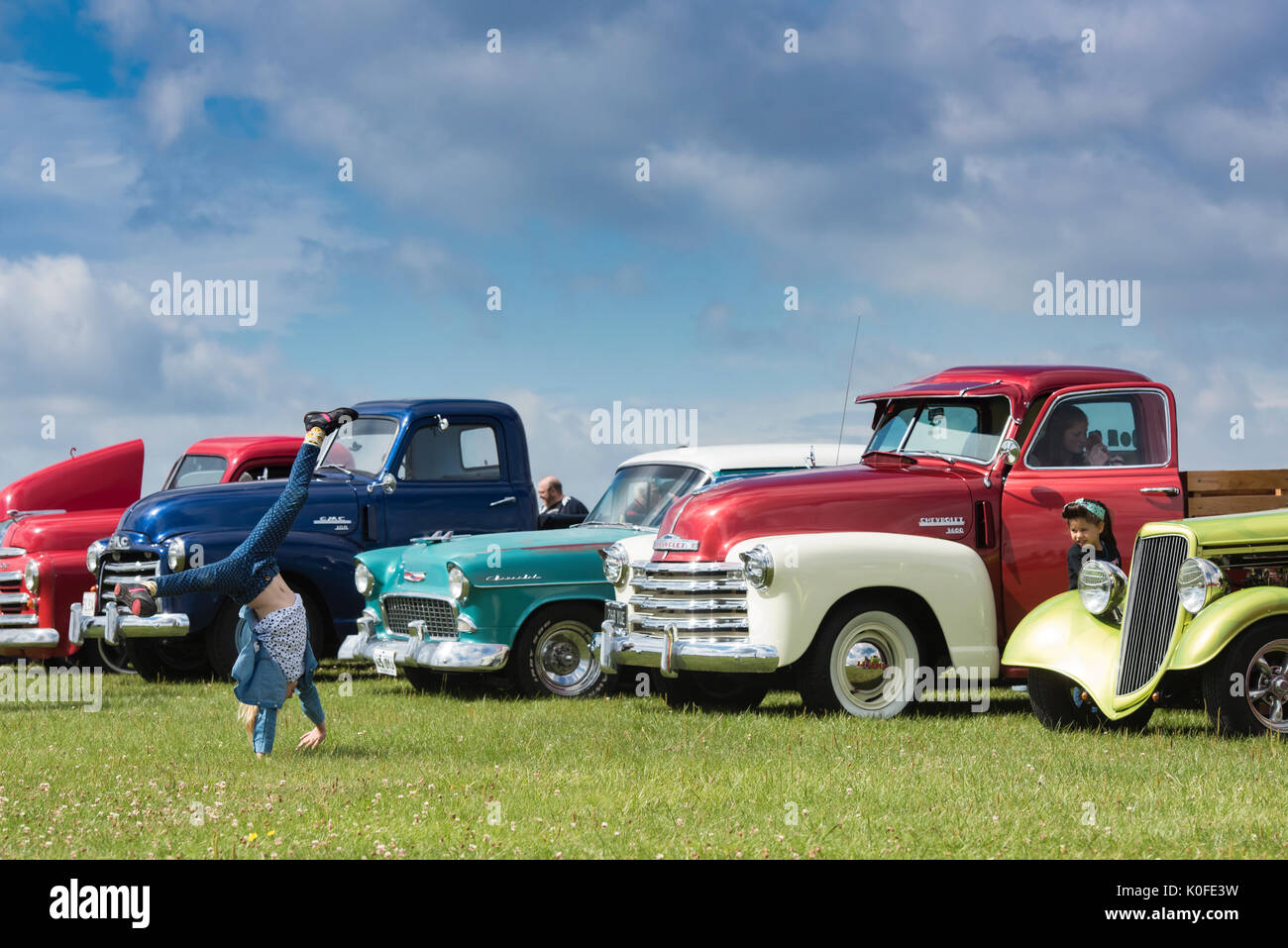 Young girl doing a handstand / cartwheel in front of 1950s Chevrolet pick up trucks at an american car show. Essex. UK Stock Photo