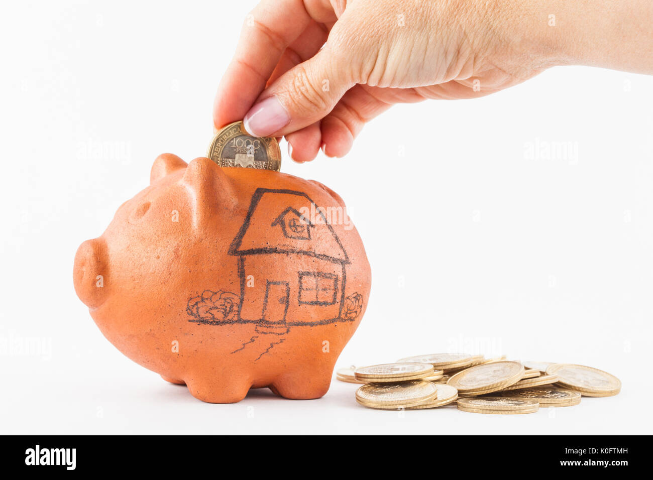 Close up of a woman saving money into a traditional clay piggy bank for a house Stock Photo