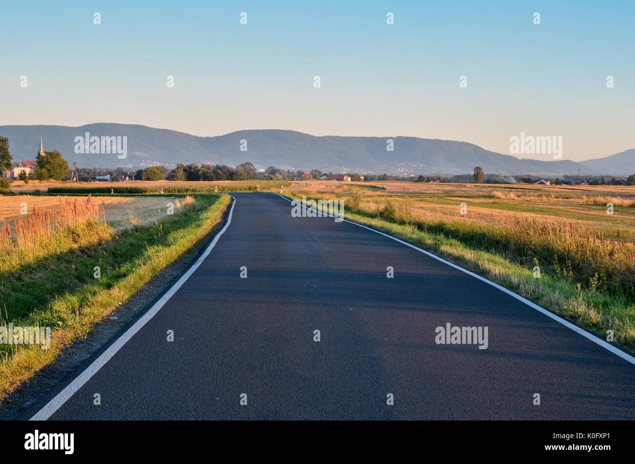 Summer rural landscape. Asphalt road with mountains and village in the ...