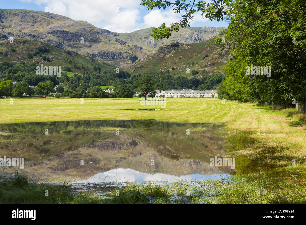 Coniston village amid the trees below Coniston Fells reflected in a standing rainwater pool in meadows near the northern shore of Coniston Water Stock Photo