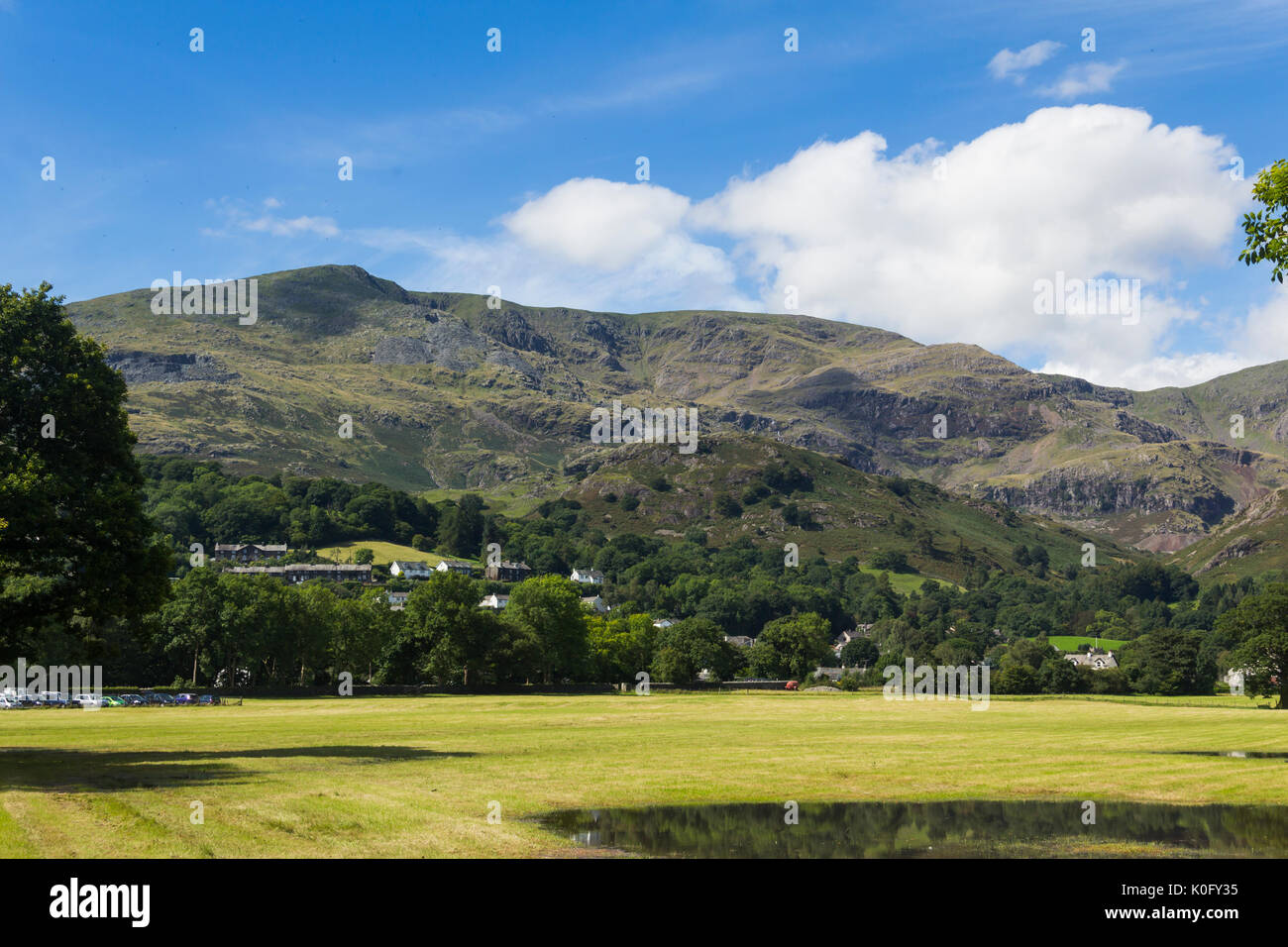 Coniston village amid the trees below Coniston Fells with the Old Man of Coniston rising to its 803 metre (2,634 feet) peak. Stock Photo