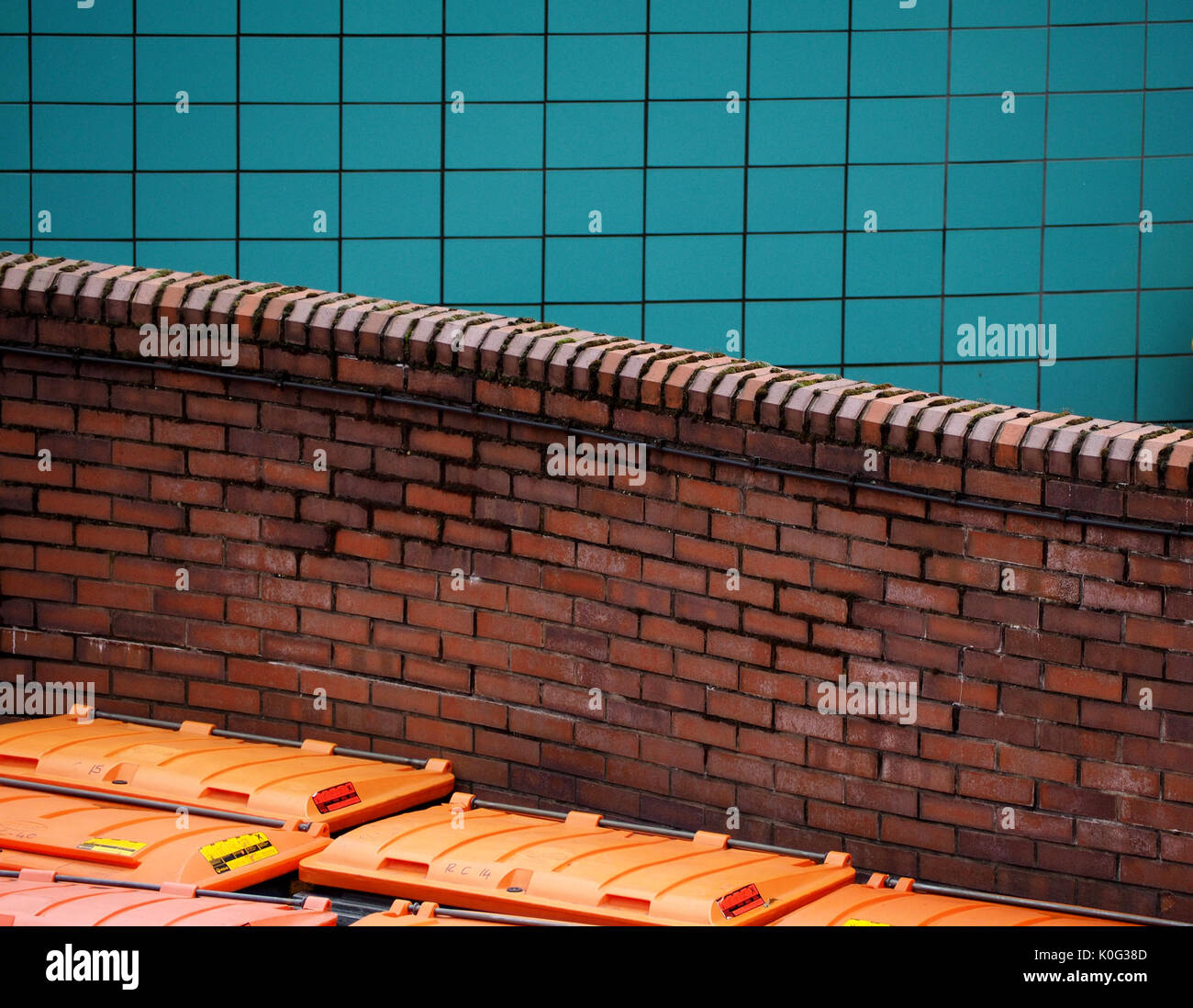 curved red brick wall behind orange waste bins with blue tiled wall in the background in Sheffield, West Yorkshire, England UK Stock Photo