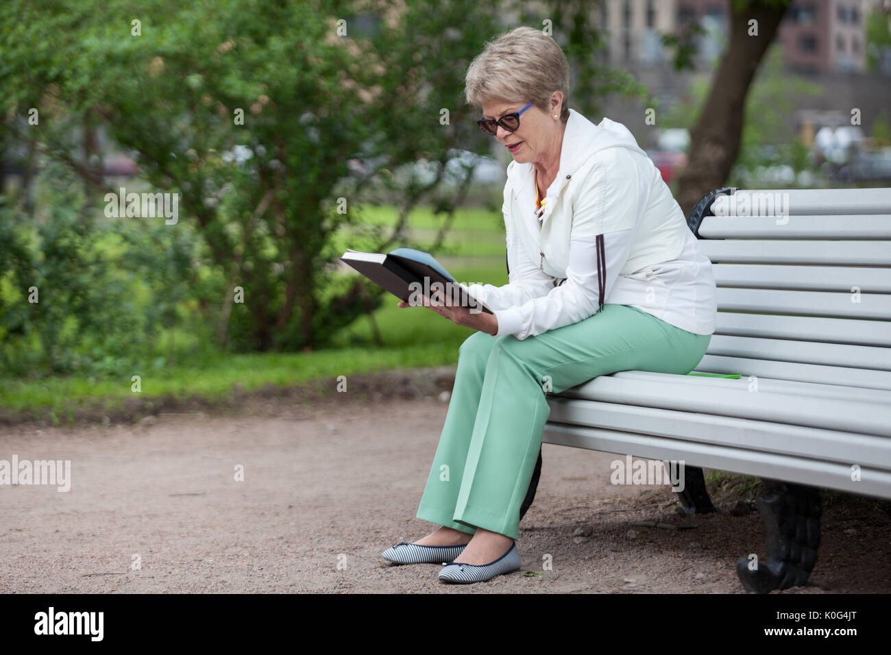 An elderly woman enthusiastically reading a book in the park on a bench, copy space Stock Photo