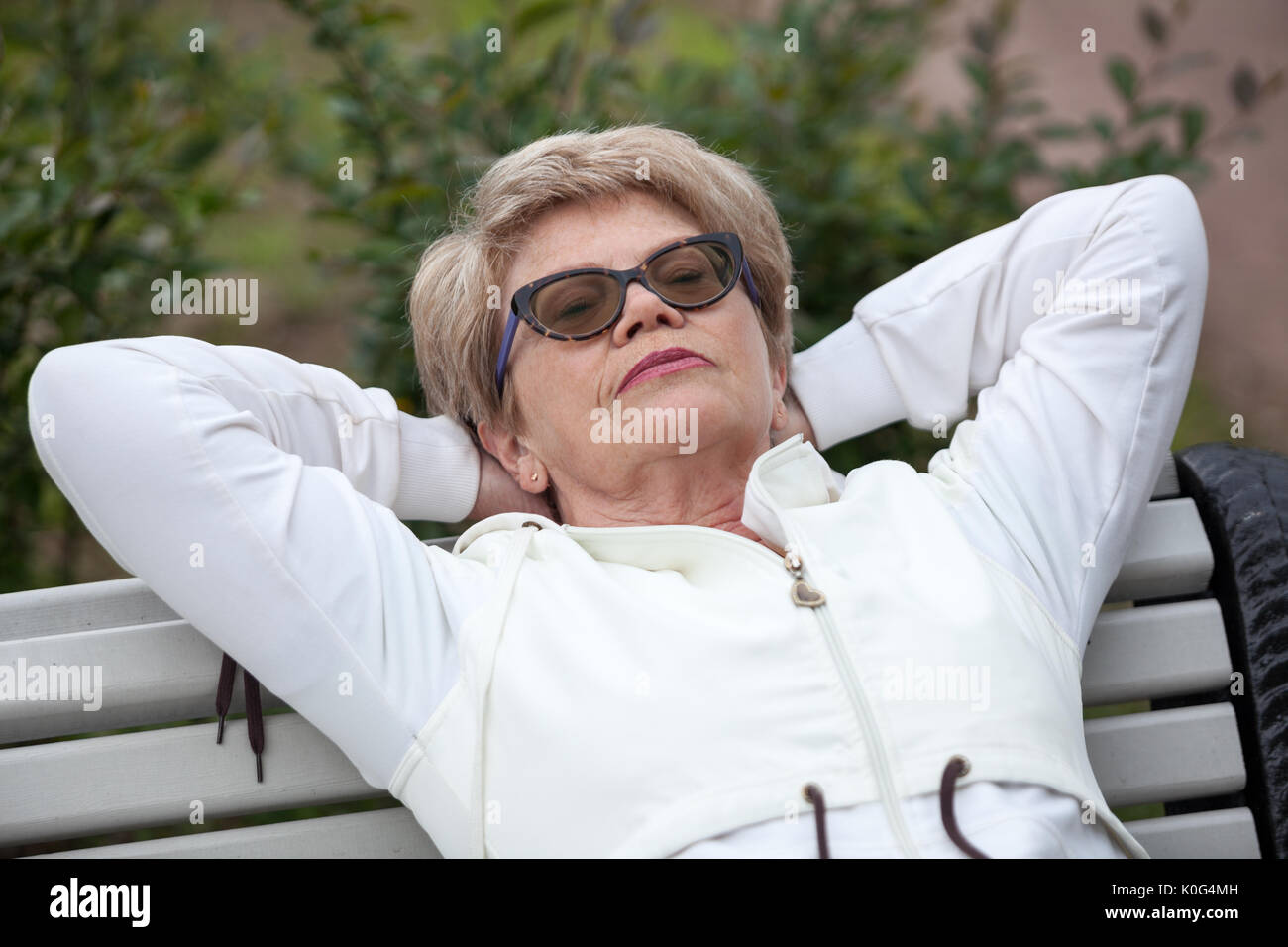 Senior woman in sports suit laying back on the bench in park after jogging Stock Photo