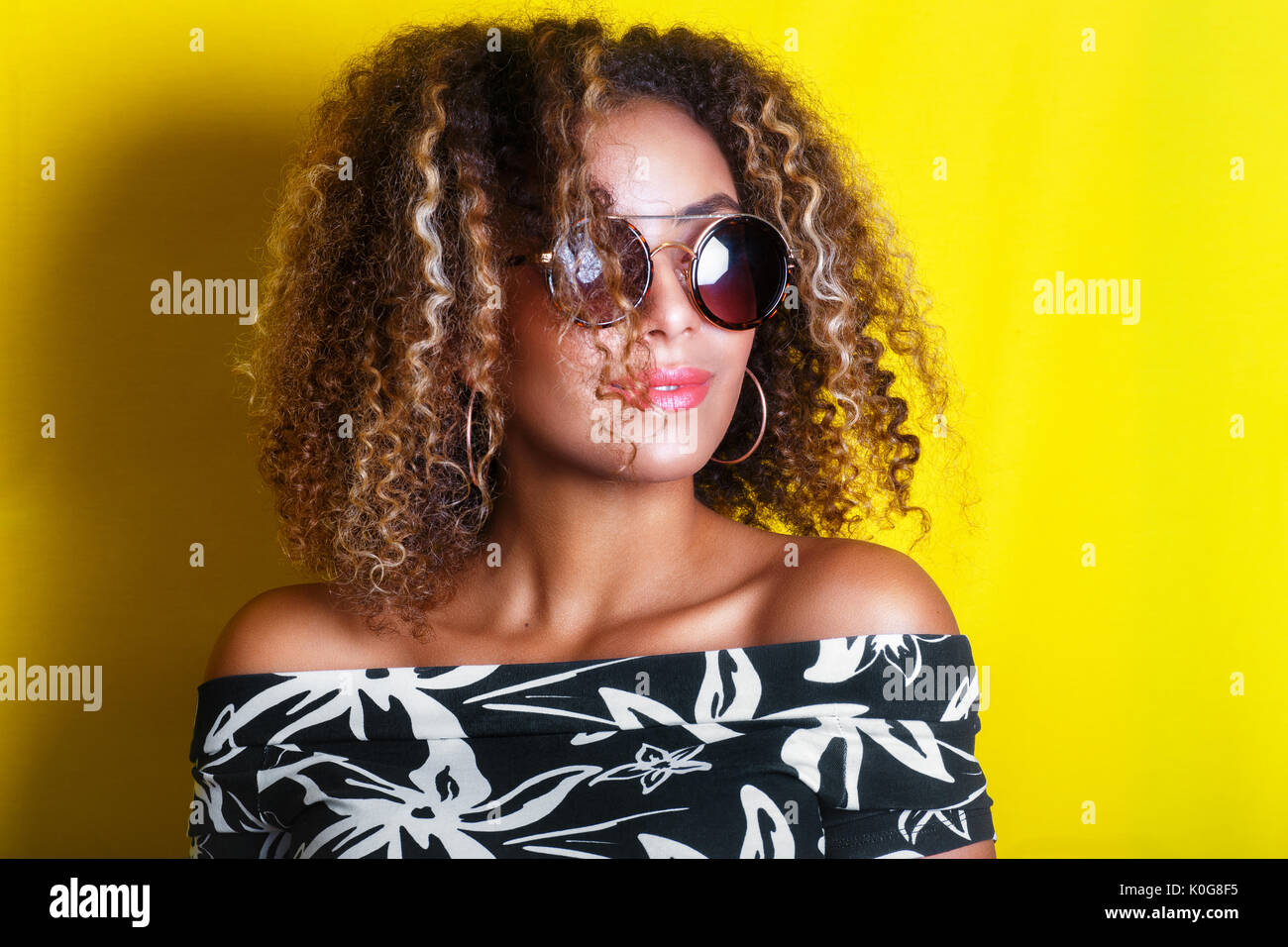 portrait indoors of a young afro american woman in sunglasses. Yellow background. Lifestyle. Stock Photo