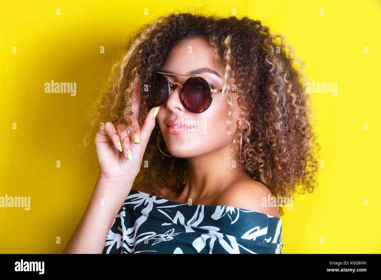 portrait indoors of a young afro american woman in sunglasses. Yellow background. Lifestyle. Stock Photo