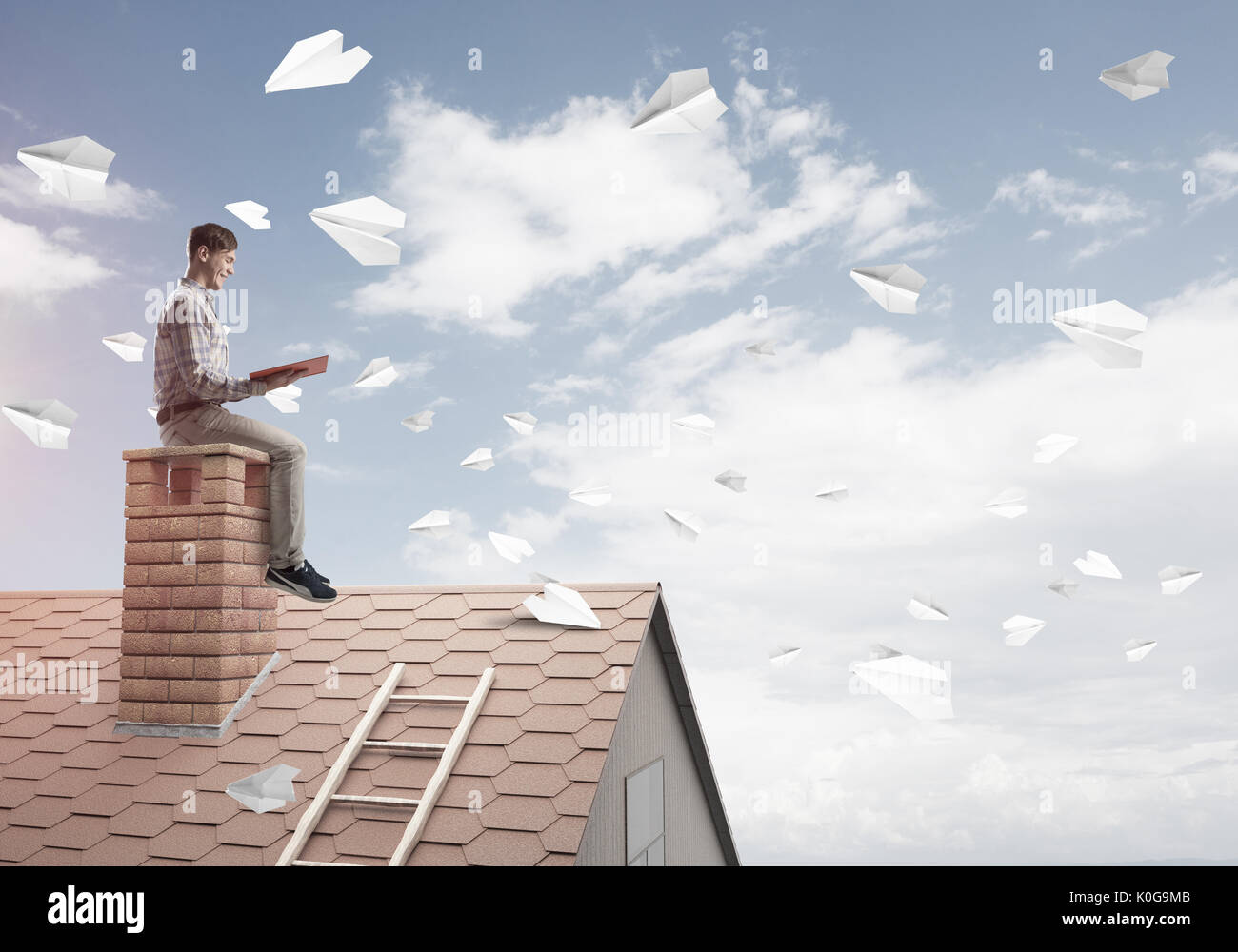 Man on brick roof reading book and paper planes flying in air Stock Photo