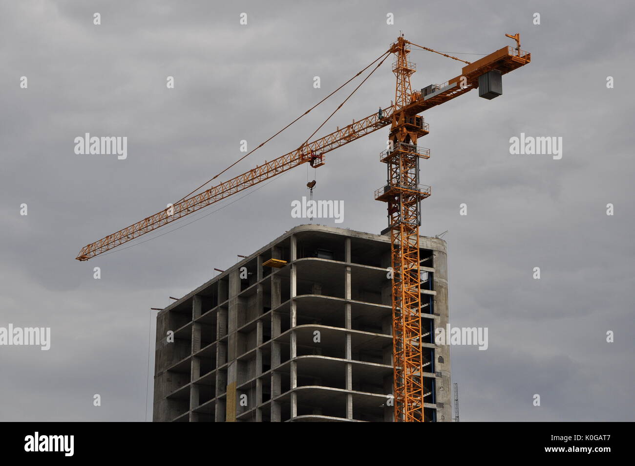 Upper part of a constructed tall building with a tower crane jib over the roof against dramatic cloudy sky. Stock Photo