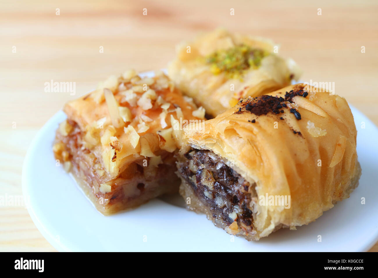 Closed up Three Types of Baklava Sweets on White Plate Served on Wooden Table, Blurred Background Stock Photo