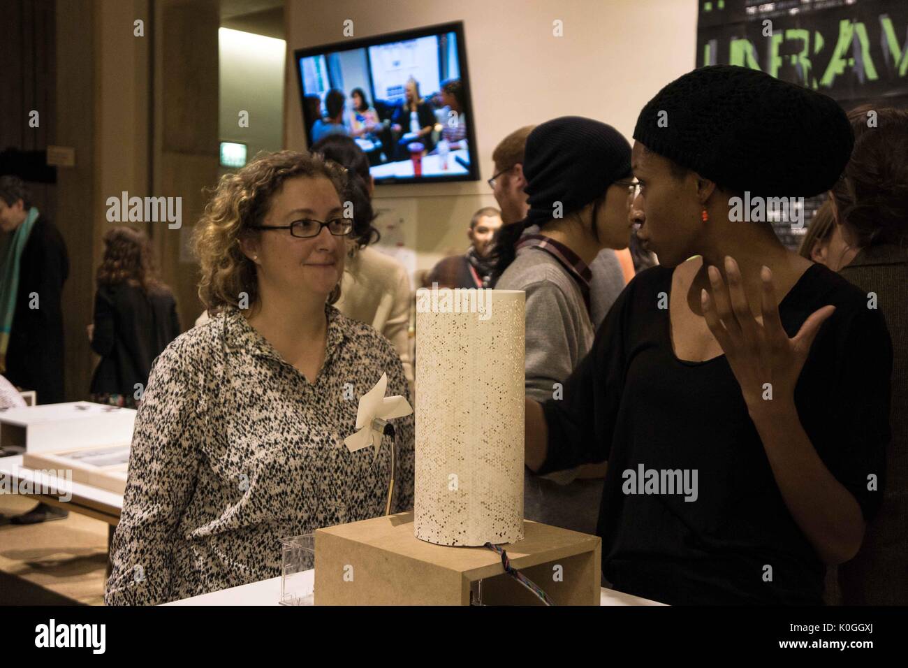 A college student and an older woman stand in front of a piece of artwork displayed on a high table, the college student describes the piece of work to the woman at the Unravel the Code Opening at The Johns Hopkins University Sheridan Libraries, 2016. Courtesy Eric Chen. Stock Photo