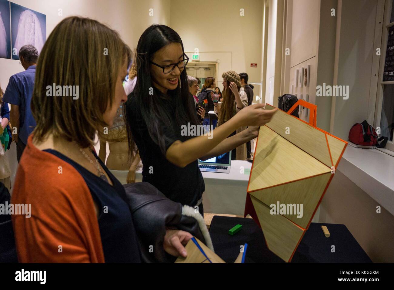 Two attendees look closely at a piece of artwork, the younger girl is holding up the artwork and observing it at the Unravel the Code Opening at The Johns Hopkins University Sheridan Libraries, 2016. Courtesy Eric Chen. Stock Photo