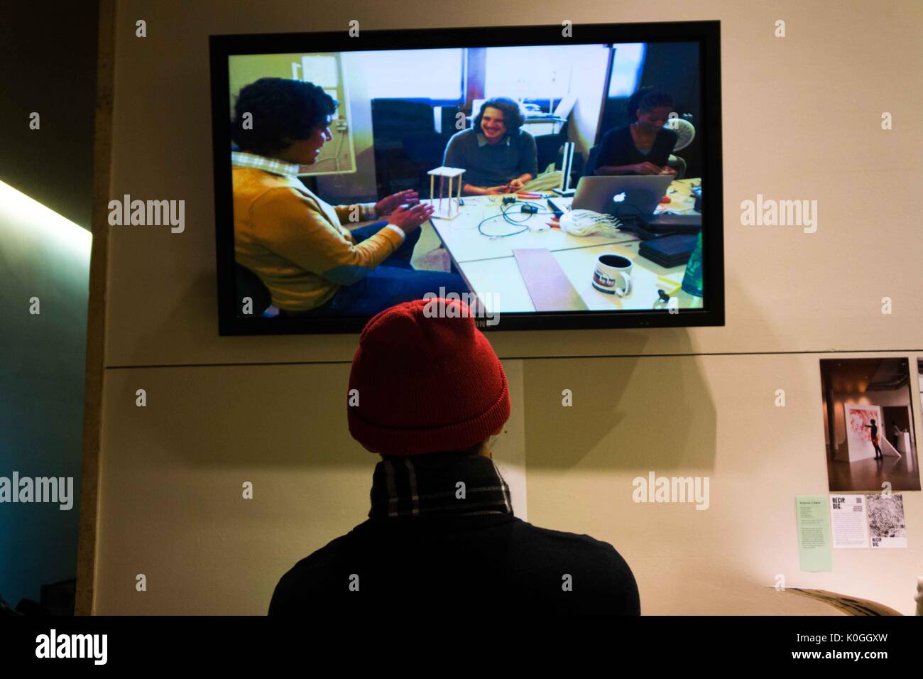 A attendee looks ahead at a television screen that is playing a video that revolves around art at the Unravel the Code Opening at The Johns Hopkins University Sheridan Libraries, 2016. Courtesy Eric Chen. Stock Photo