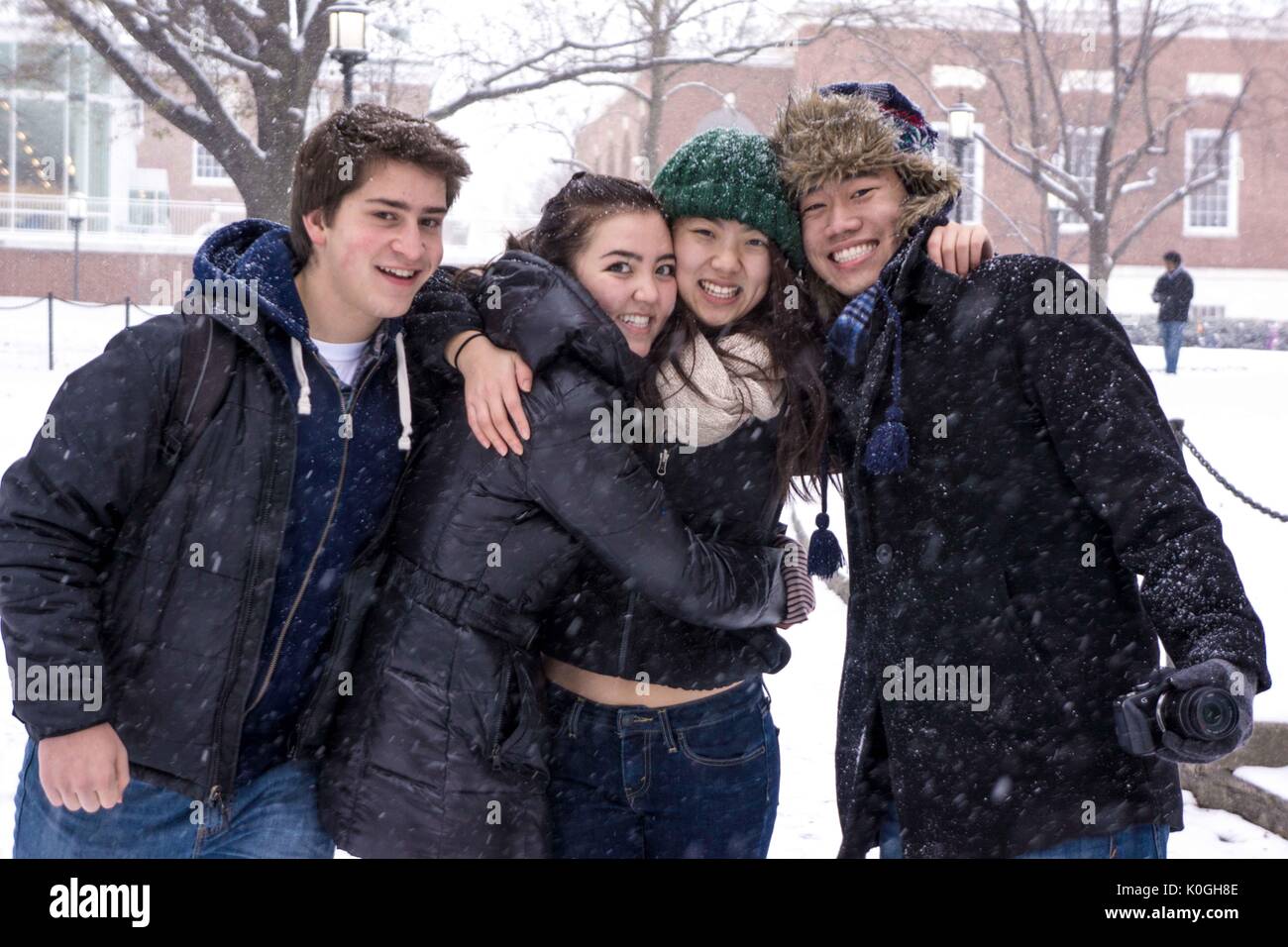 Four freshman college students at the Johns Hopkins University gather together and smile in front of the Milton S. Eisenhower Library as snow falls on the Homewood campus in Baltimore, Maryland, 2014. Courtesy Eric Chen. Stock Photo