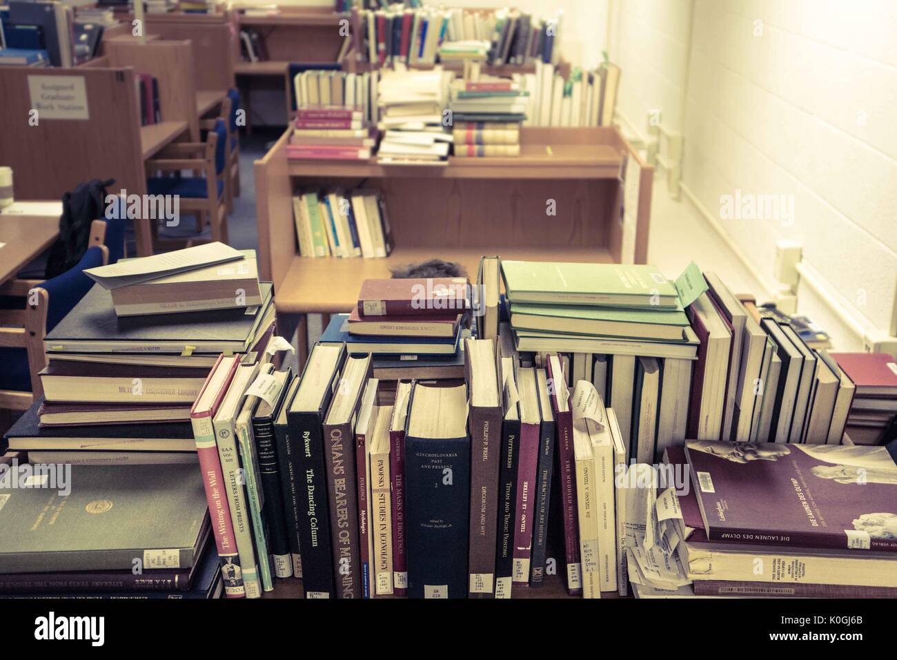 A graduate student sits at his work space, surrounded by piles of books, in the Milton S. Eisenhower Library on the Homewood campus of the Johns Hopkins University in Baltimore, Maryland, 2015. Courtesy Eric Chen. Stock Photo