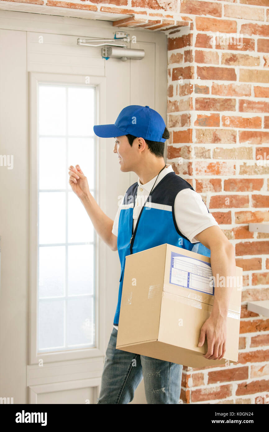 Side view of young delivery man knocking on door Stock Photo