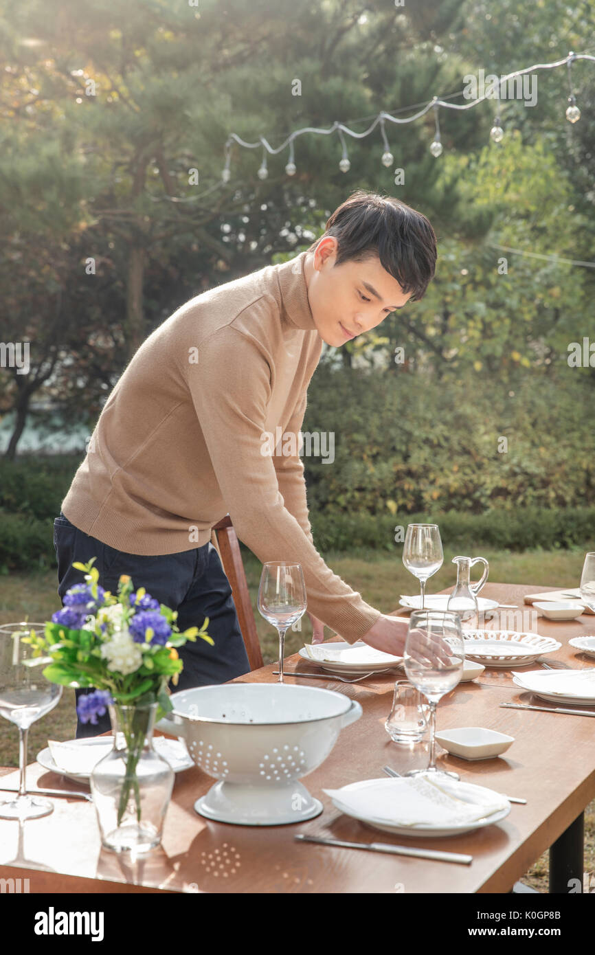 Side view of young smiling man setting a table for party at garden Stock Photo