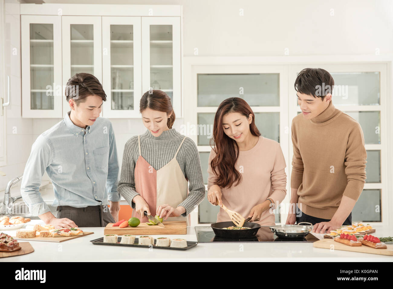 Young smiling people preparing for dessert for party in kitchen Stock Photo