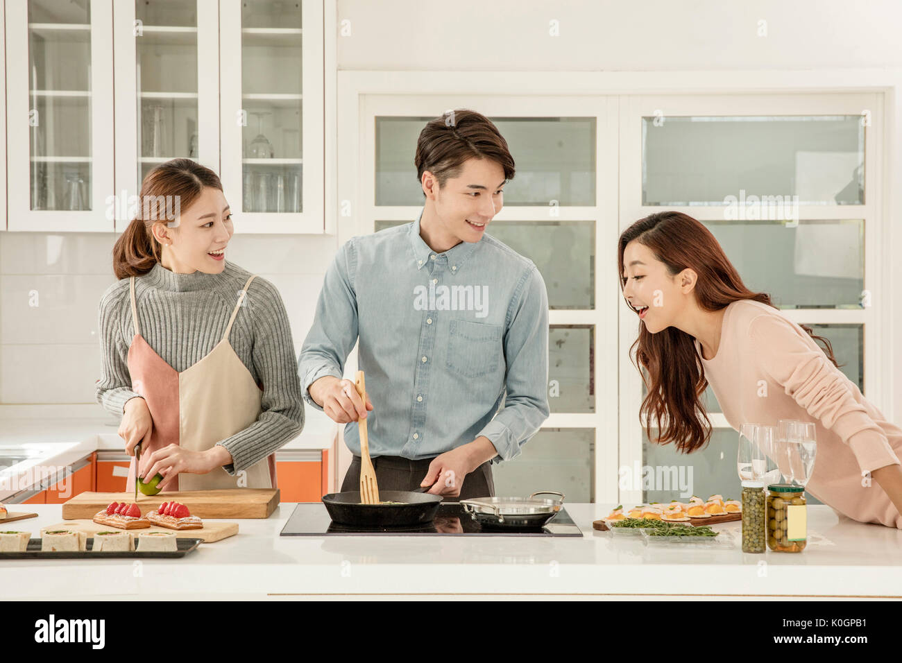 Young smiling people preparing for food for party in kitchen Stock Photo
