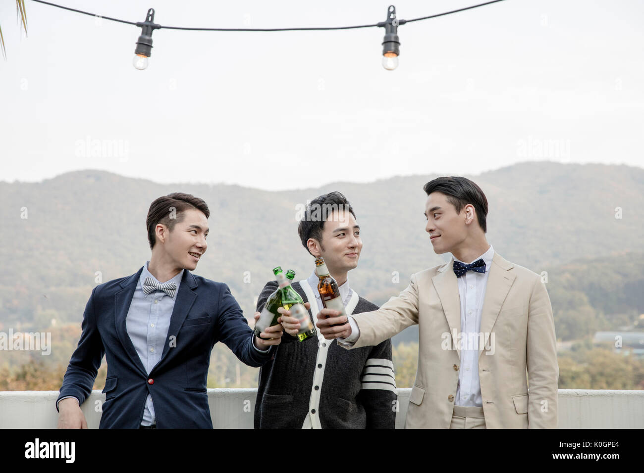 Portrait of three young men toasting with beer bottles at rooftop Stock Photo