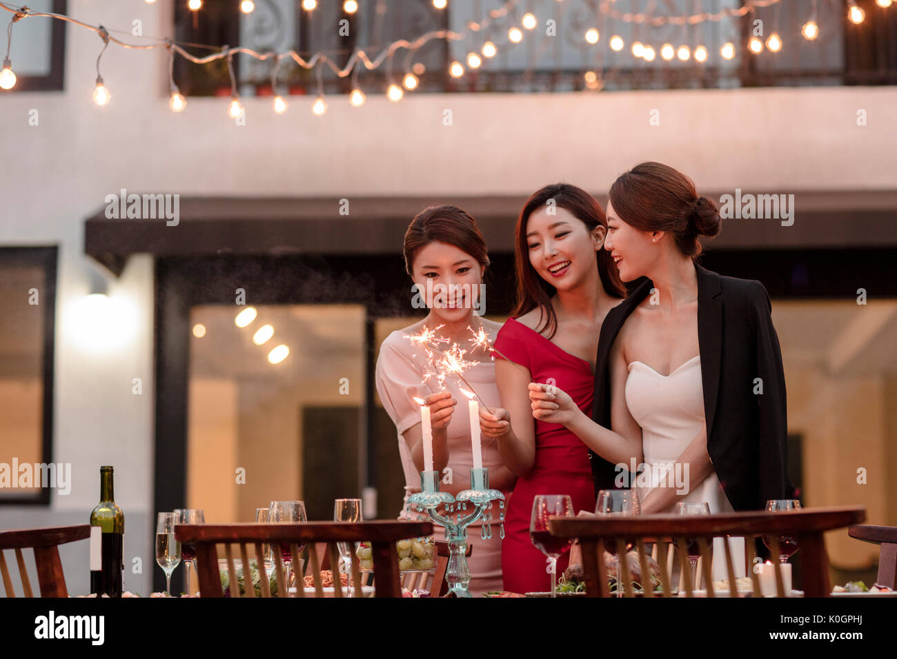 Three young smiling women with firecrackers enjoying a party at garden in the evening Stock Photo