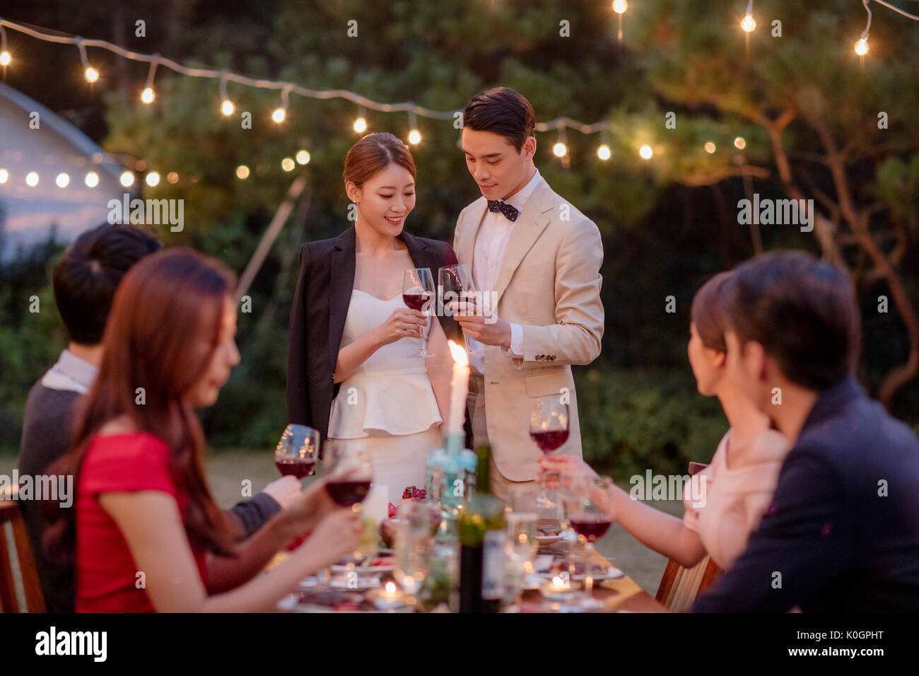 Smiling couple with wine glasses posing and their friends enjoying a party outdoors in the evening Stock Photo