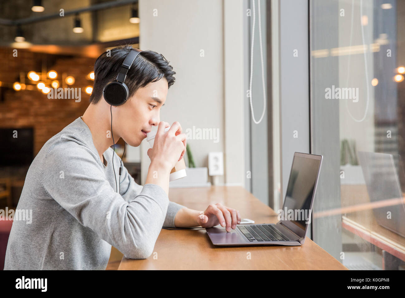Side view portrait of young businessman with headphones using a notebook computer at cafeteria Stock Photo