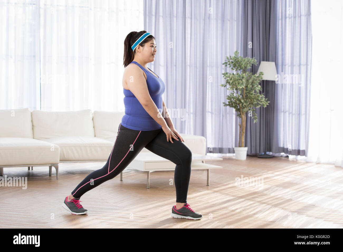 Side view of young smiling fat woman exercising indoors Stock Photo