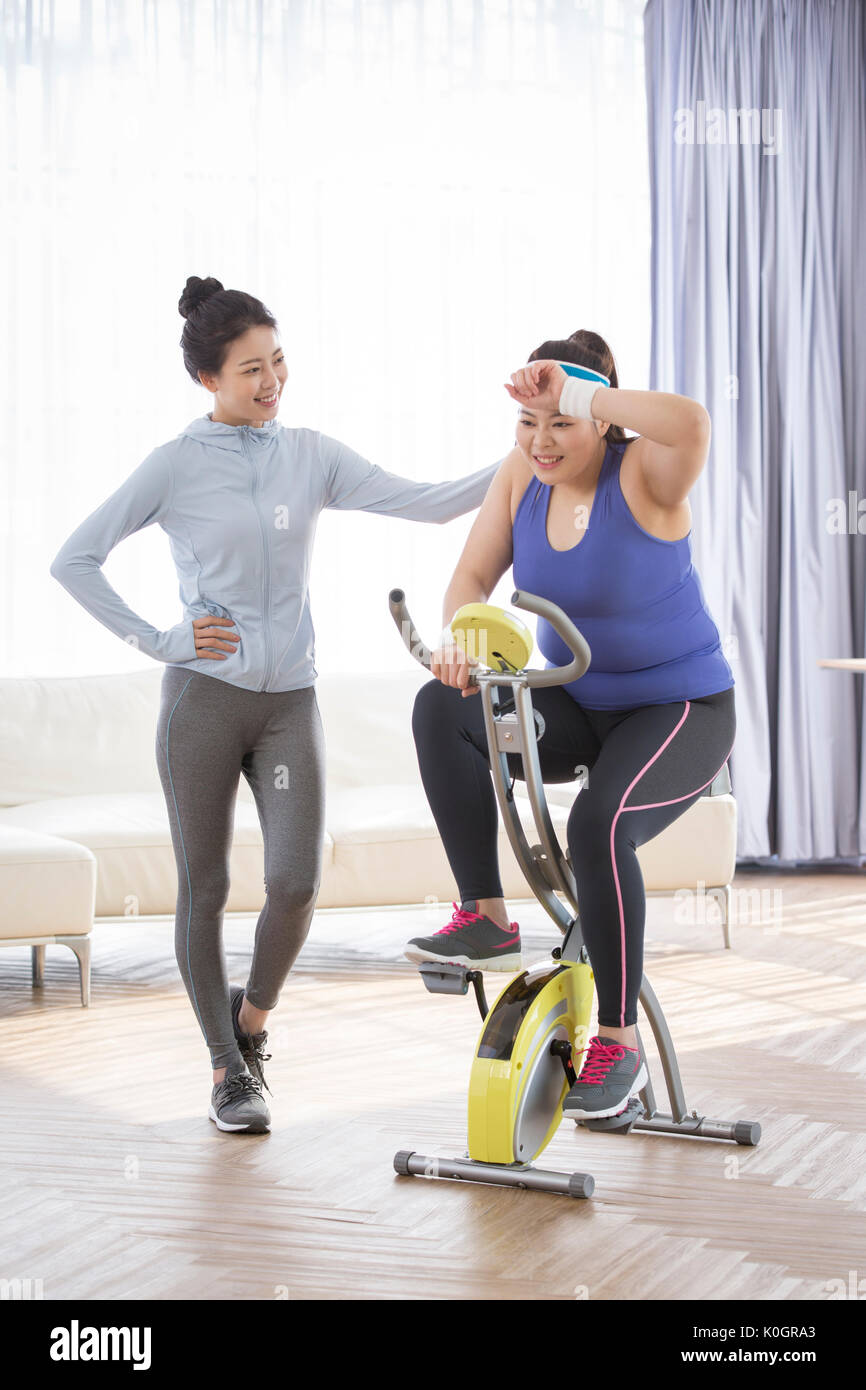 Young smiling slim female trainer helping young fat female trainee ...