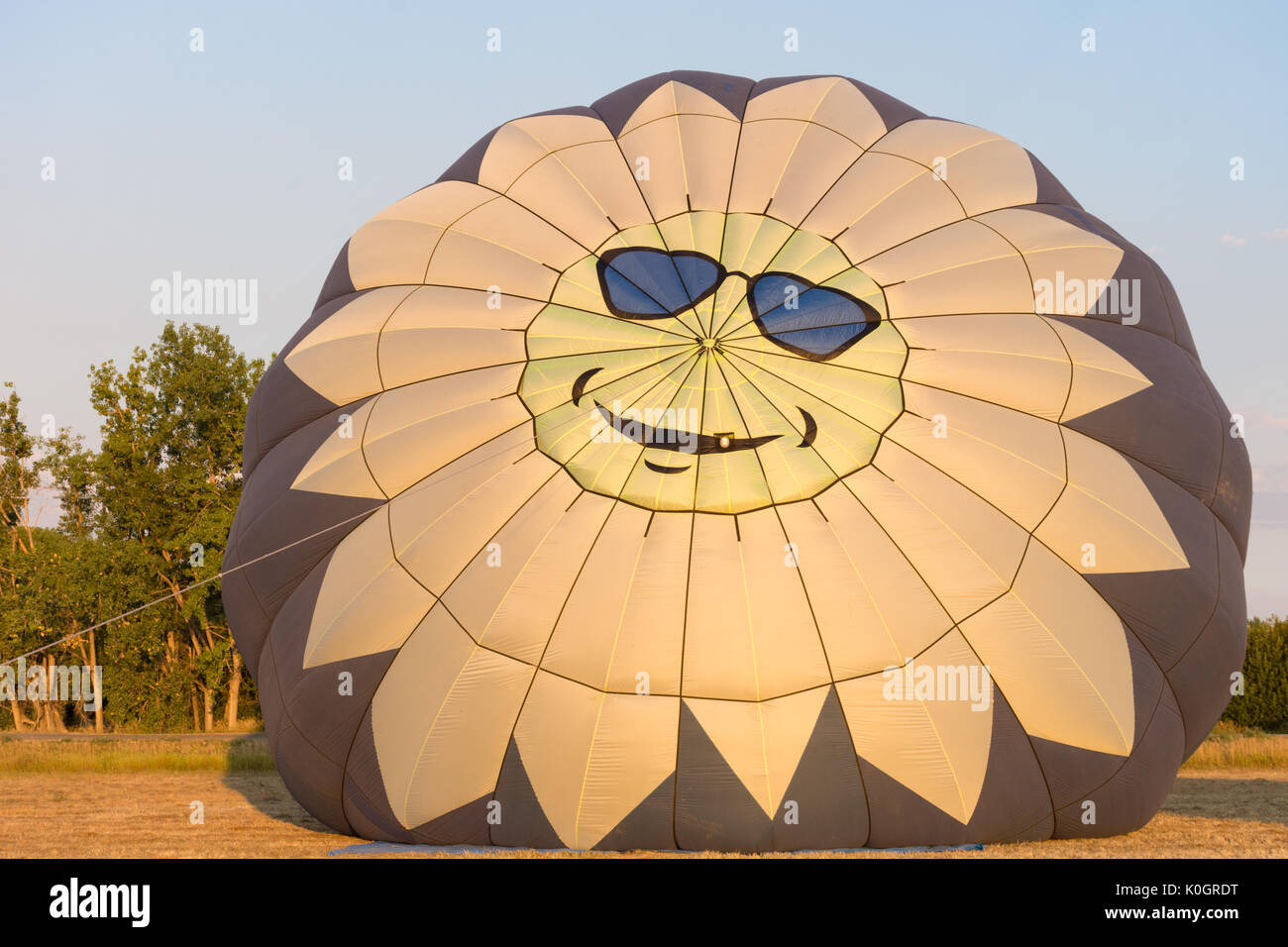 A hot air balloon with a happy sun face with blue sunglasses on the top, The balloon is being inflated at sunrise. Stock Photo