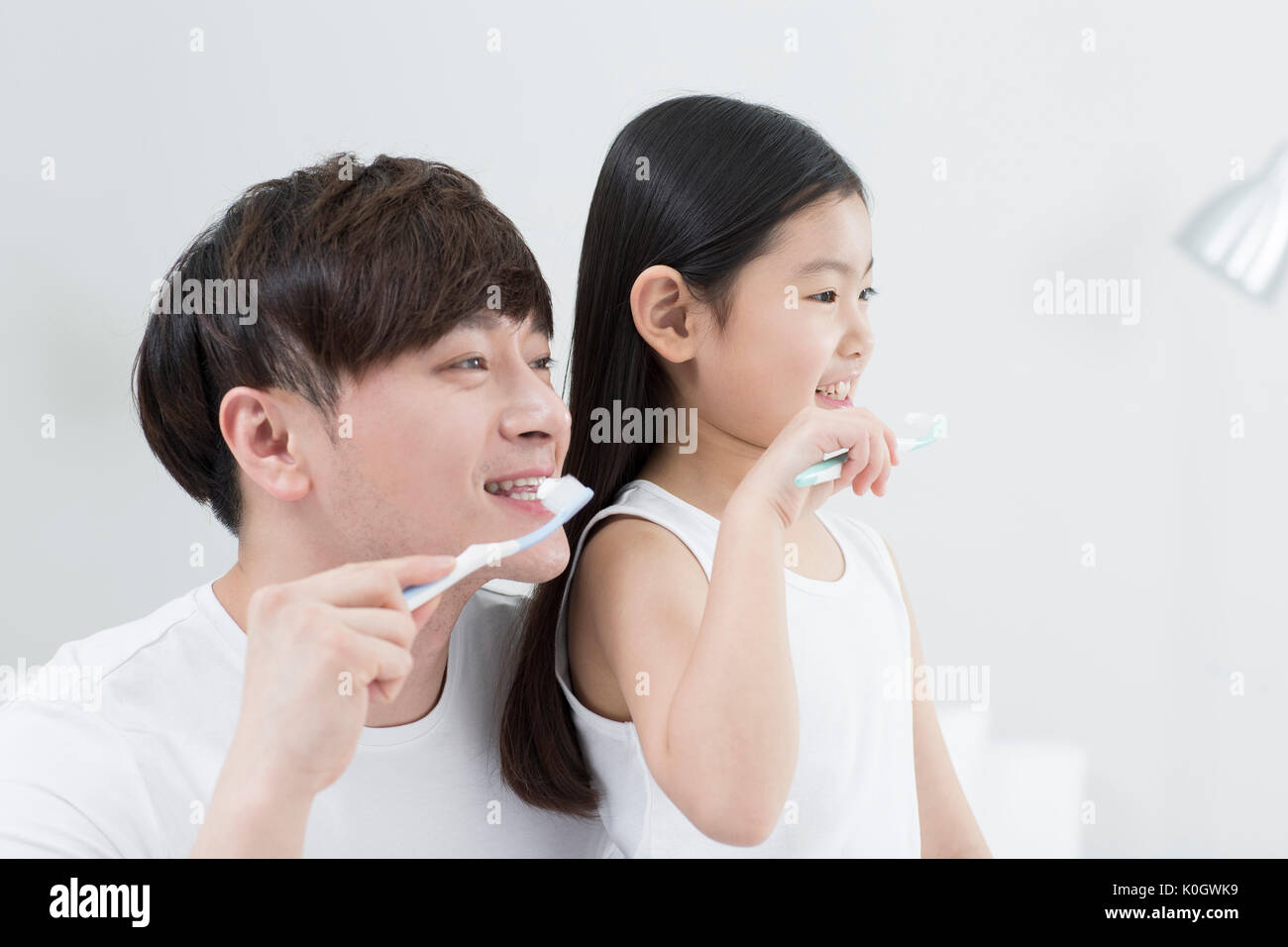 Side view portrait of smiling father and girl brushing teeth together Stock Photo