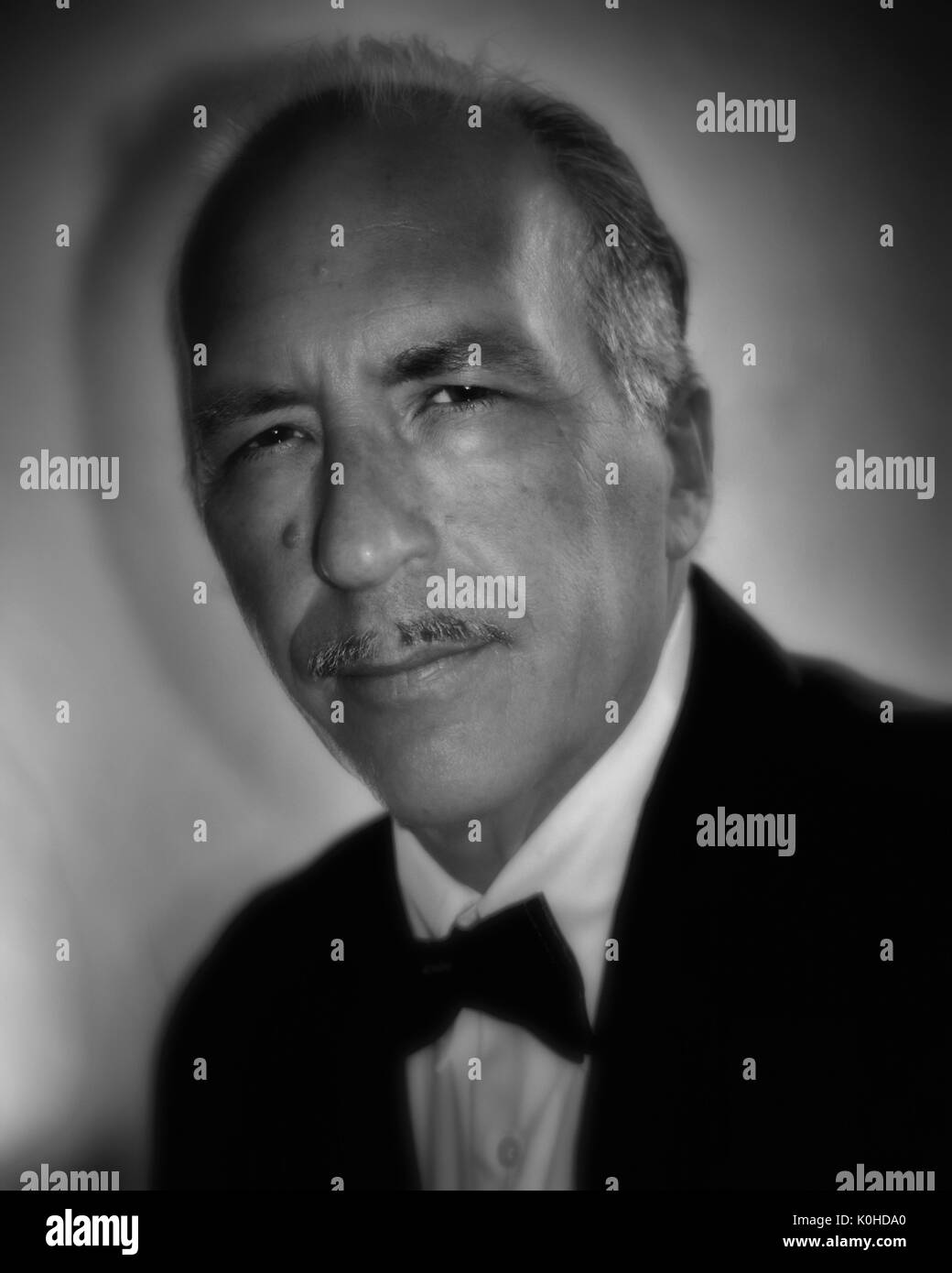 Portrait of an older white man in formal dress tuxedo, slicked back hair and pencil mustache, looking at camera with black/ white old hollywood feel Stock Photo