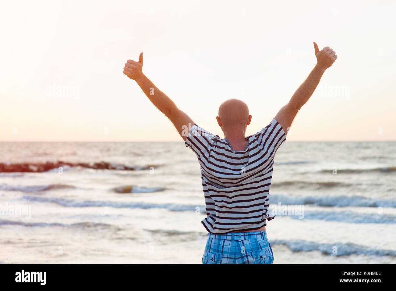 Happy man raises his arms up against the sea Stock Photo