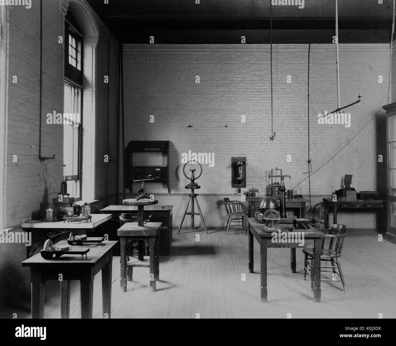 Photograph of the Johns Hopkins physics undergraduate electricity and magnetism lab, with a wooden floor and brick desks and wooden stools, with large windows on the walls and miscellaneous instruments and tools on the desks. 1900. Stock Photo