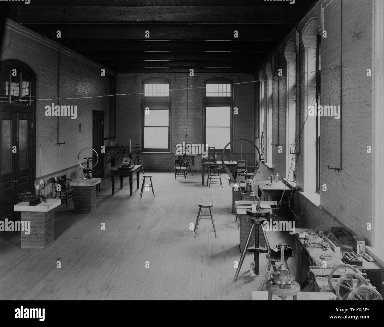 Photograph of the Johns Hopkins physics undergraduate electricity and magnetism lab, with a wooden floor and brick desks and wooden stools, with large windows on the walls and miscellaneous instruments and tools on the desks. 1900. Stock Photo