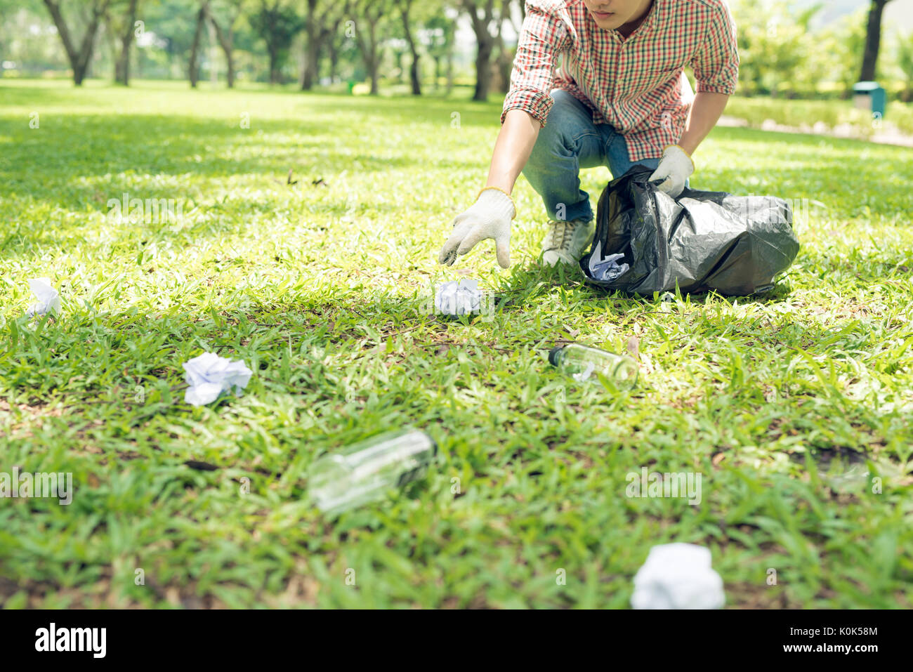 Young man crouching to waste and picking it up in bin bag Stock Photo