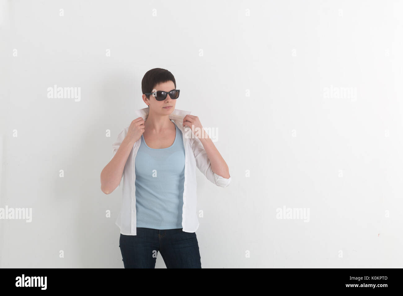 Portrait of young girl in jeans and sunglasses with short hair holding a white shirt collar. Stock Photo