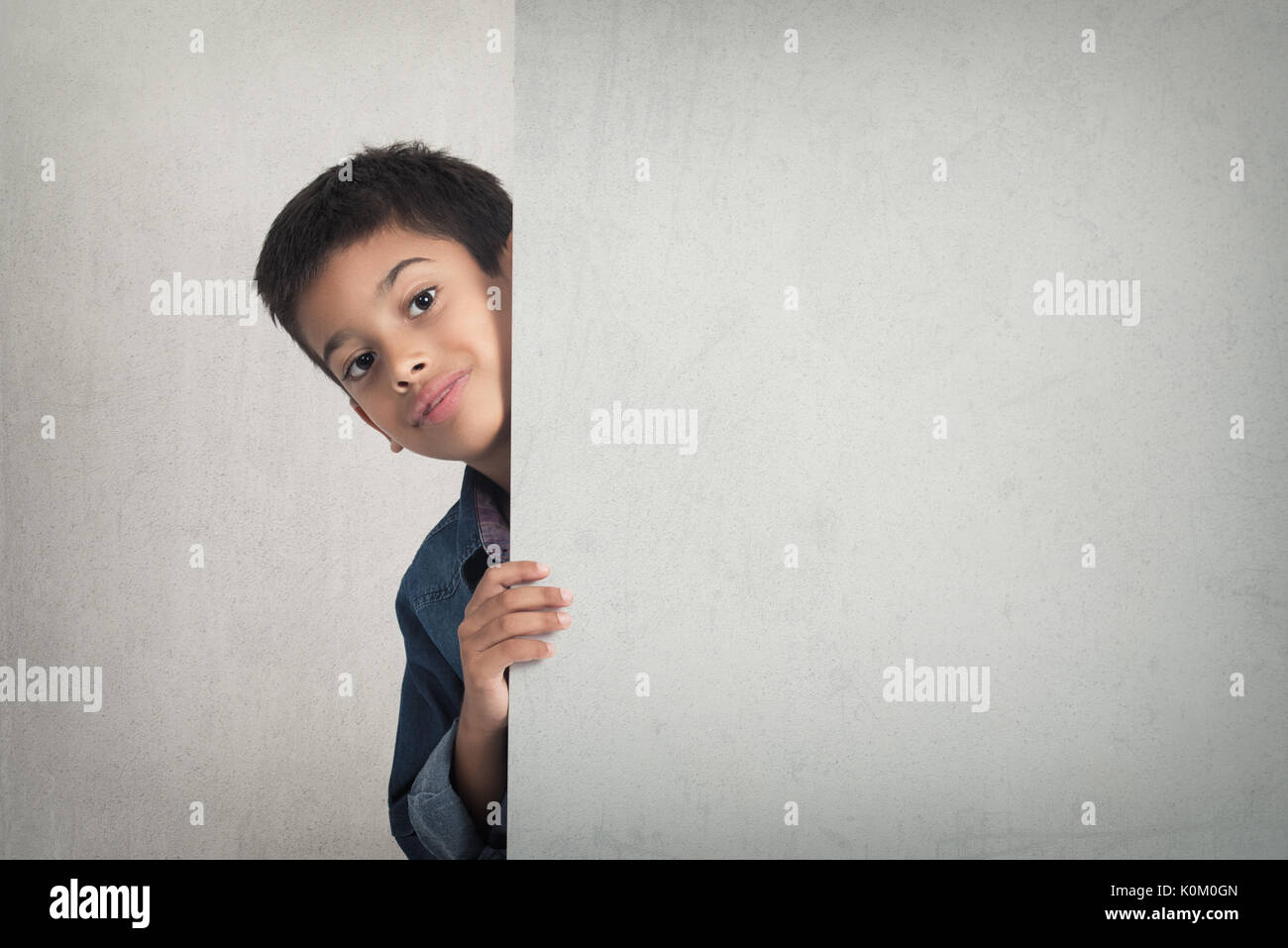 Cute boy looking from behind blank advertising board Stock Photo