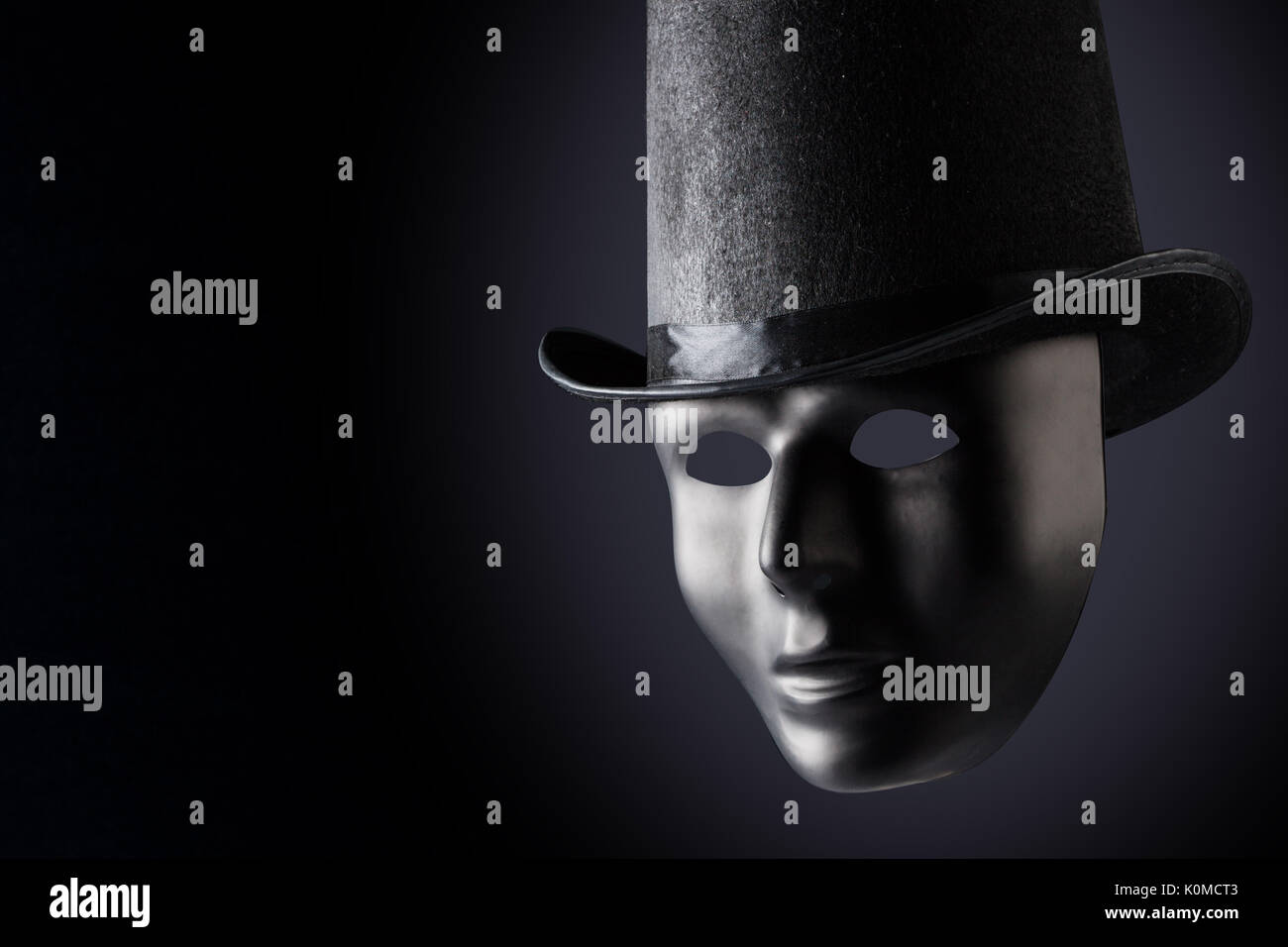 Black mask face closeup wearing black top hat on black background with copy space. Social masking and mystery concept Stock Photo