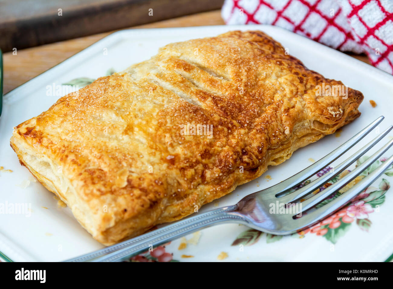 A closeup of a single Apple pastry served onto a side plate, with a red and white kitchen cloth to the top part of the image Stock Photo