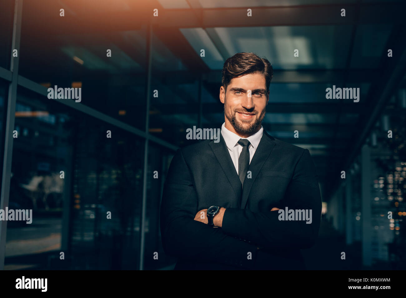 Portrait of smiling young businessman standing with his arms crossed ...