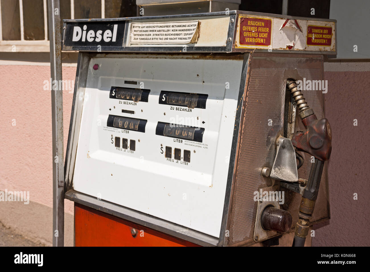 Old diesel petrol pump in Austria. Filling station in front of pink colored house. Warnings in German for safe refueling: stop engine, no open fire. Stock Photo