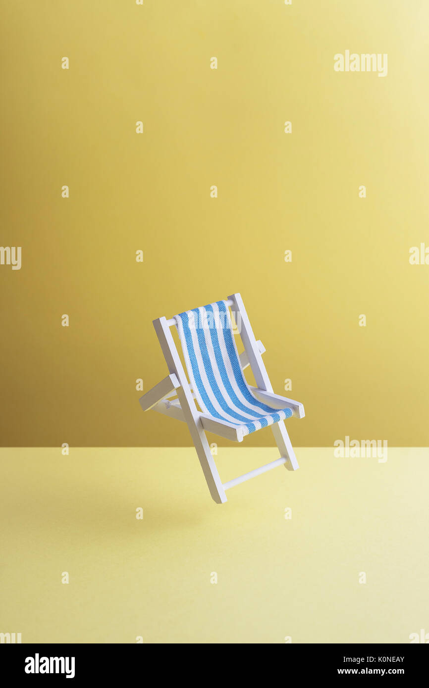 Single beach chair hovering in the air in front of yellow ground, 3D Rendering Stock Photo