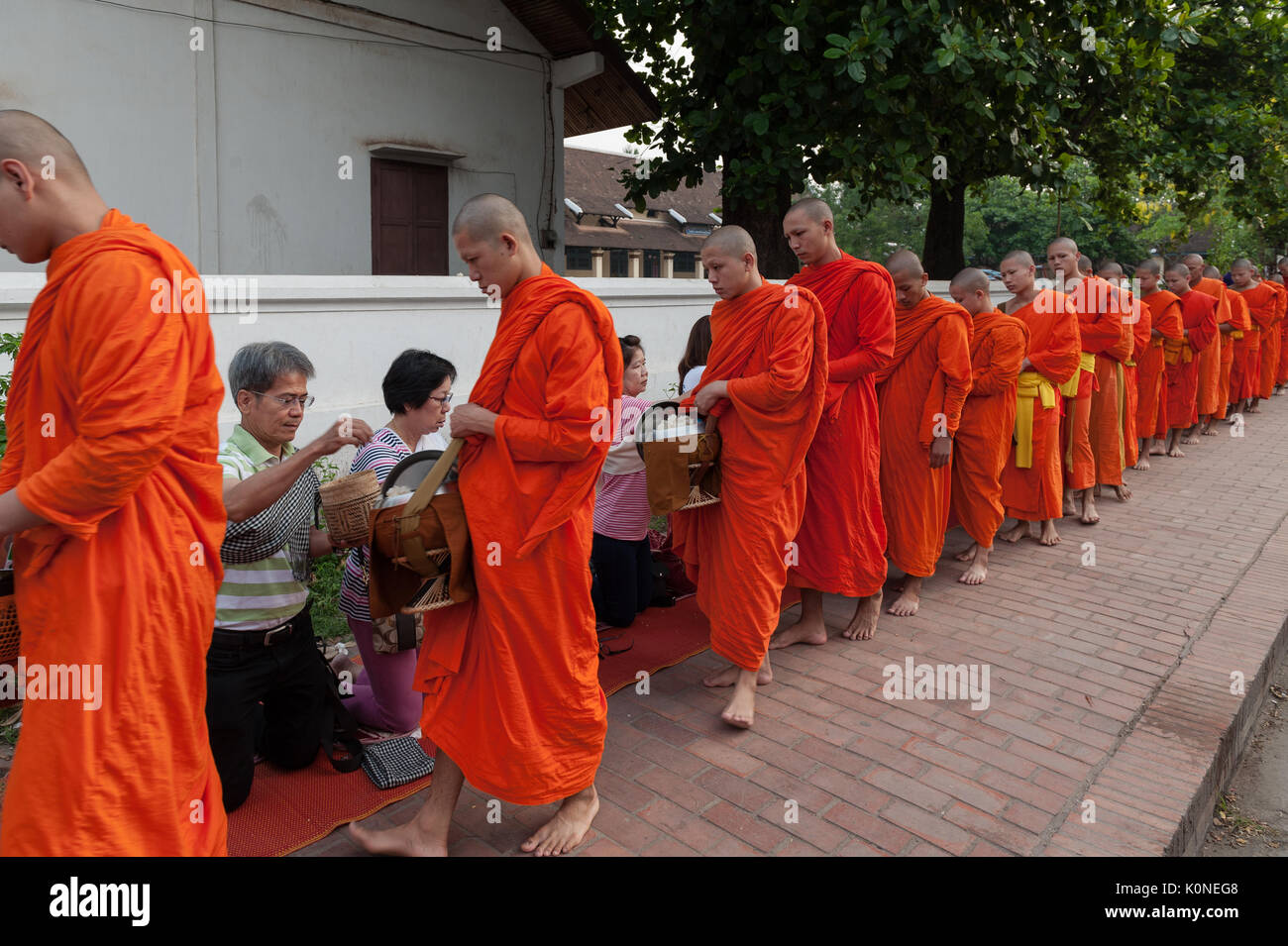 A procession of barefooted monks collects alms along the streets of Luang Prabang, Laos. The most common gifts offered are sticky rice, bananas, sweet Stock Photo
