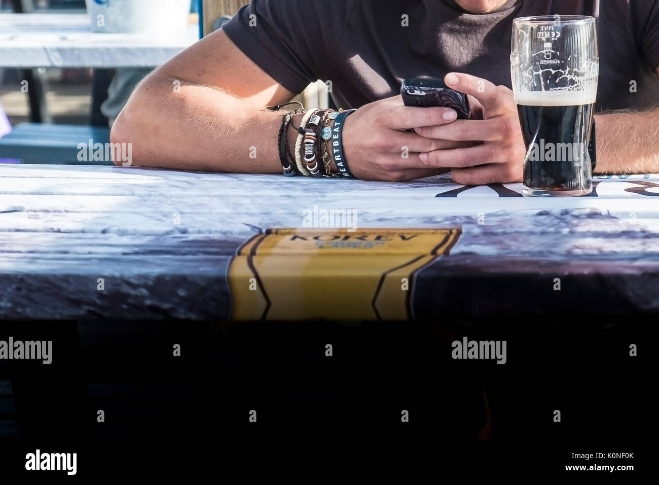 A man sitting at a table using his smartphone and wearing various bracelets on his arm. Stock Photo