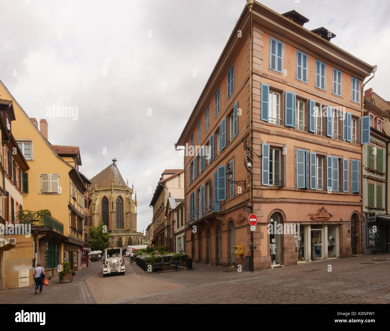 Old wide street with tourist train and people walking, paving stones and old building in perspective. Colmar, France. Stock Photo