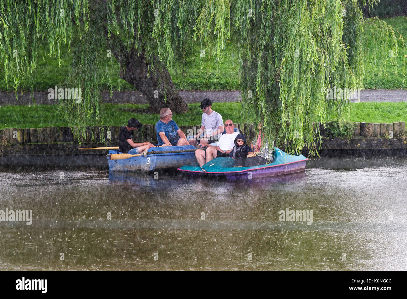 Holidaymakers on a boating lake sheltering under a willow tree from a torrential downpour. Stock Photo