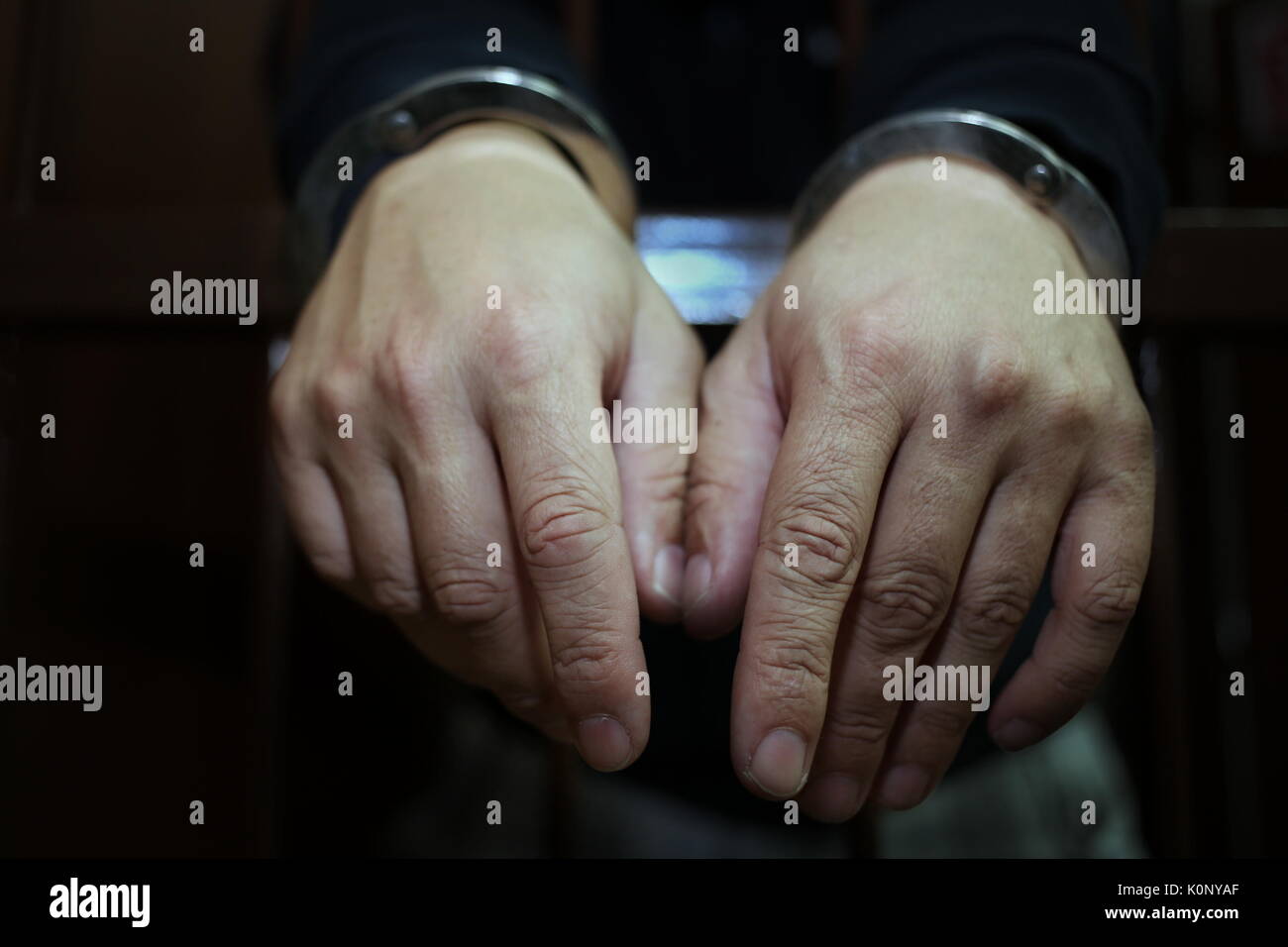 Abstract. Hands of the prisoner on a steel lattice close up. Prison, man in handcuffs. Detail of hands with steel handcuffs. Stock Photo