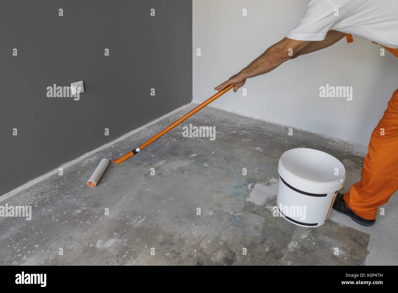 The hand of a man holding a roller and puts primer on concrete floor. Interior of a house under construction Stock Photo