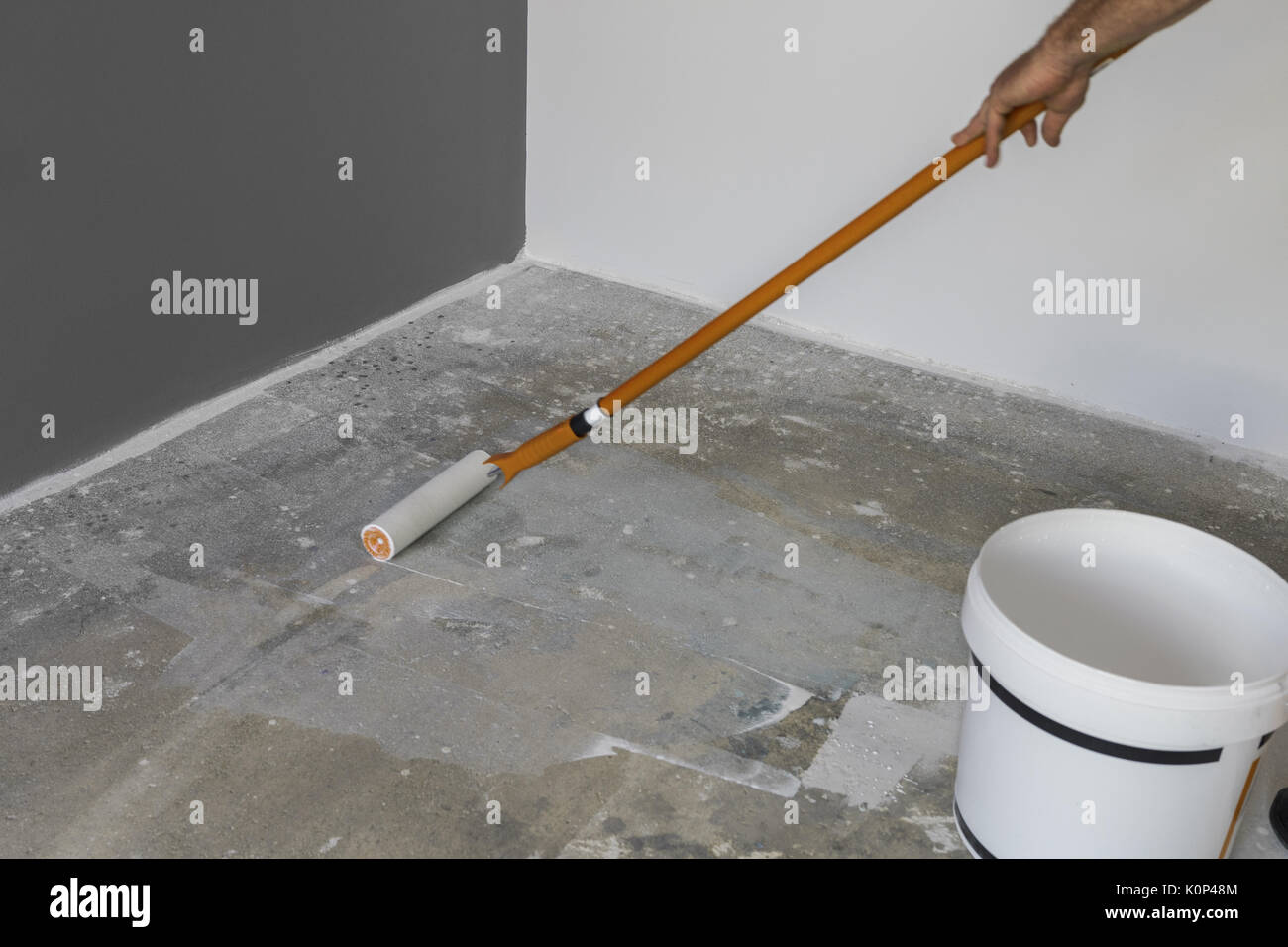The hand of a man holding a roller and puts primer on concrete floor Stock Photo